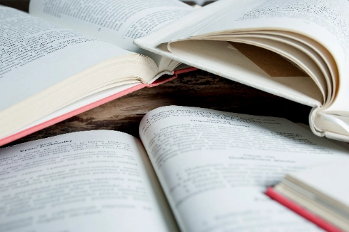 Primer plano de varios libros abiertos y apilados, representando la base teórica y el estudio constante necesarios para dominar el trading.