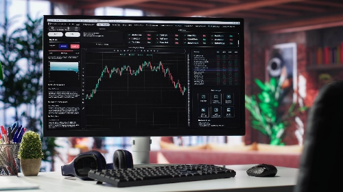 Un monitor de computadora en un escritorio ordenado muestra una plataforma de trading con un gráfico financiero central