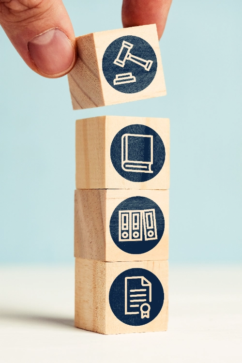 Una mano coloca el último bloque de una torre vertical de cuatro cubos de madera, cada uno con iconos legales y de oficina impresos en círculos azules