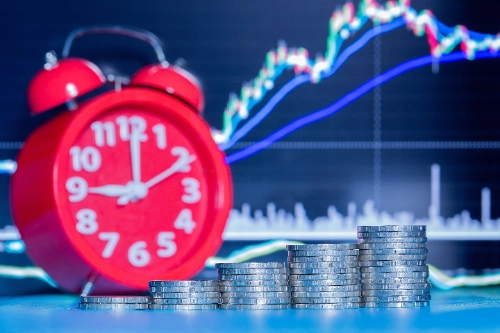 Qué significa ir largo y corto en trading: monedas apiladas junto a un reloj representando inversión y timing