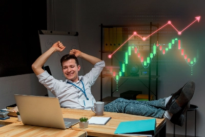 se muestra a un joven empleado sonriente y relajado en su oficina, con los pies sobre el escritorio y los brazos arriba en señal de éxito, mientras observa un gráfico financiero flotante con una tendencia ascendente.
