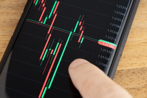 Un dedo tocando la pantalla de un teléfono inteligente que muestra un gráfico de velas financieras con valores numéricos.