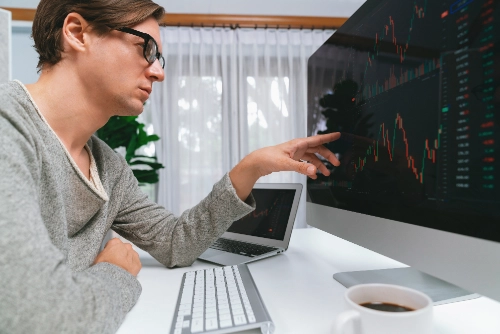 Un hombre con gafas analiza atentamente una pantalla de computadora de escritorio y señala gráficos financieros.