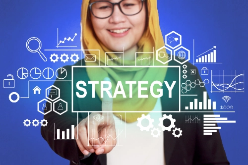 Una mujer con hiyab y gafas toca una pantalla virtual con la palabra "STRATEGY" rodeada de iconos gráficos, sobre un fondo azul.