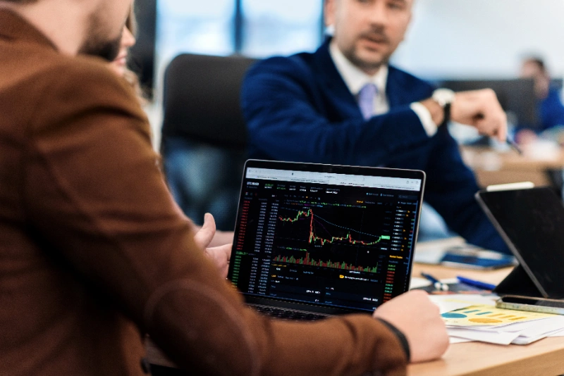 Ejecutivos en una reunión de negocios analizando gráficos bursátiles y datos financieros en un portátil.