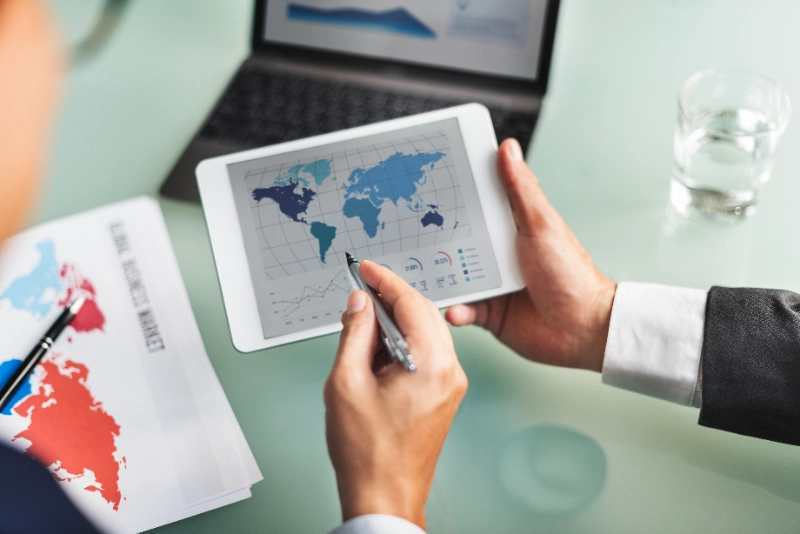 Ejecutivo analizando un mapa global de negocios y métricas de mercado en una tableta digital sobre su escritorio de trabajo