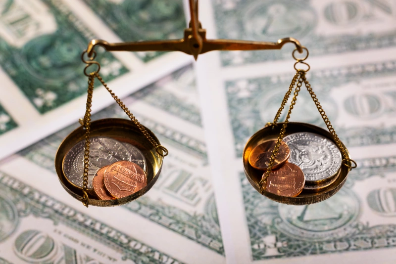 Balanza dorada de precisión equilibrando monedas de dólar y centavos sobre un fondo de billetes estadounidenses.